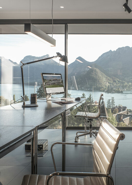 Salon avec vue sur le lac et les montagnes : Vue panoramique d'un salon moderne avec de grandes baies vitrées offrant une vue imprenable sur le lac et les montagnes à Annecy.